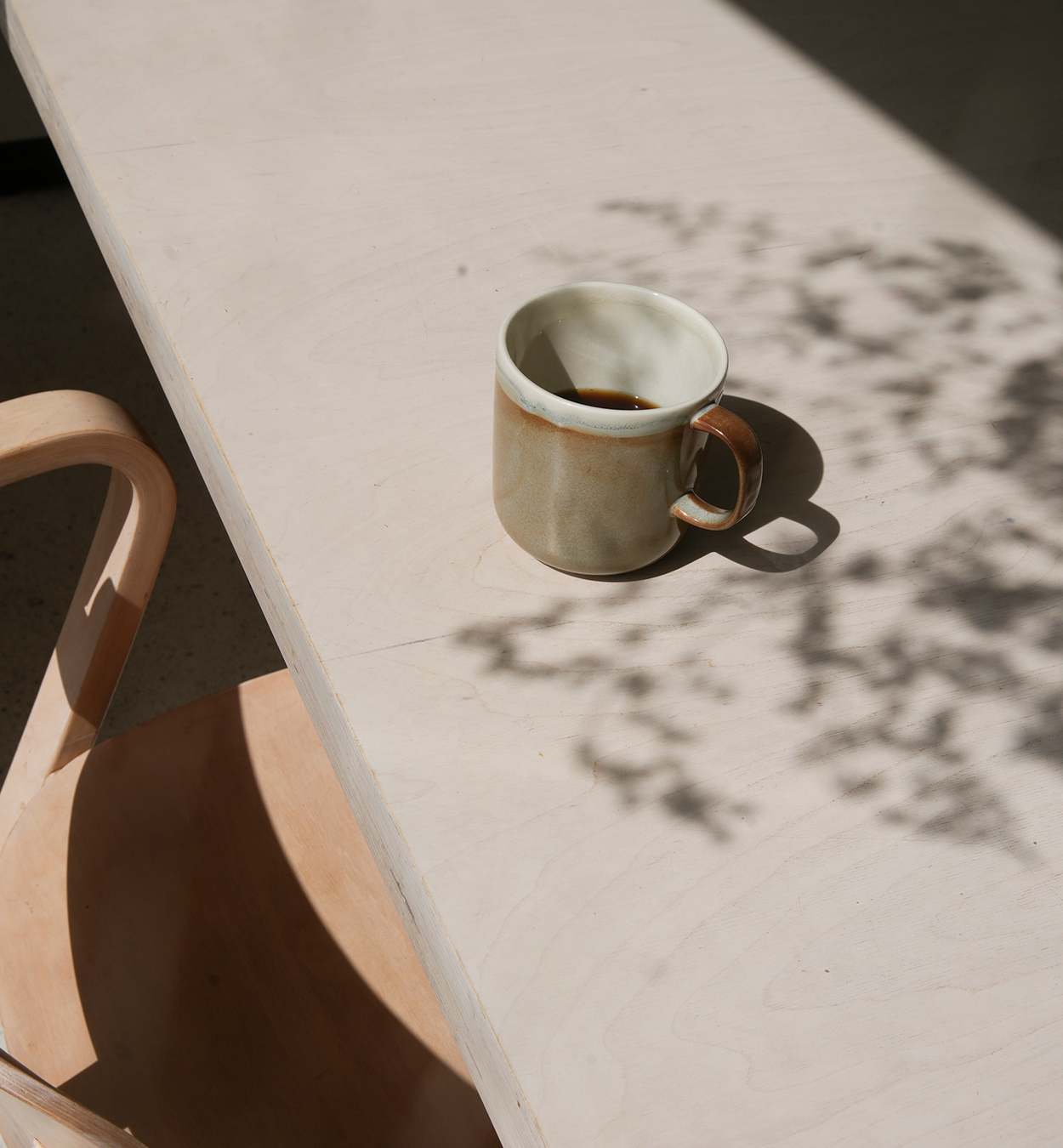 Brown ceramic mug from Tuntu tableware collection on a wooden table. Soft natural light and plant shadow.