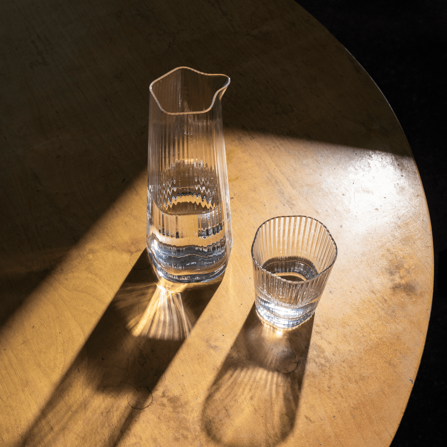 Clear striped pitcher and tumbler from Vuolle collection photographed on wooden table with delicate light reflections.